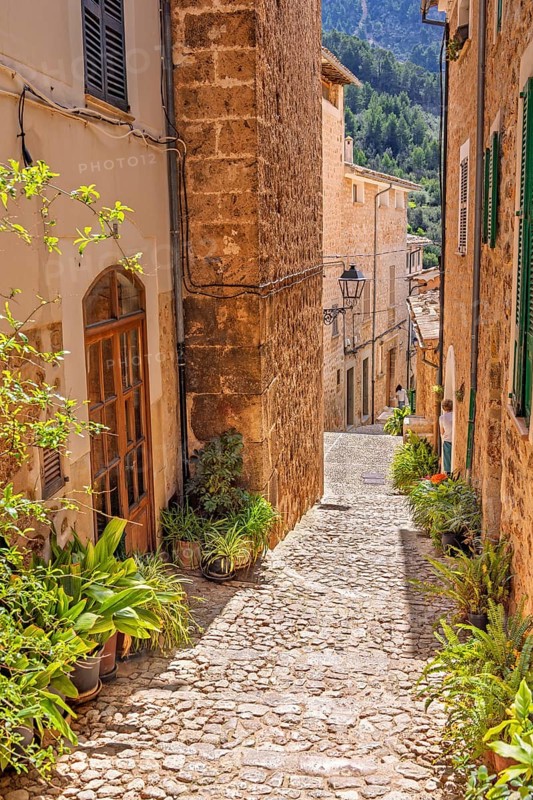 Empty cobblestone alley with beautiful stone houses a sunny hot day in an old spanish village, Fornalutx, Mallorca, Spain
