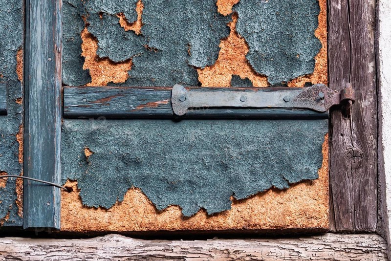Weathered detail of an old shutter with rusty hinge and peeling paint, Alsace, France