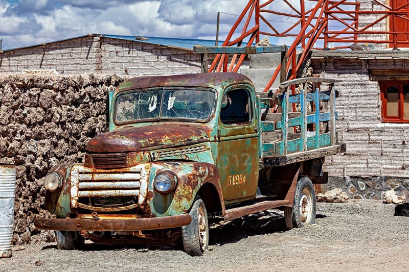 Rusty historic lorry next to an old brick building with outside stairs under a blue sky, Old lorry in a village on the edge of the Salar de Uyuni in Bolivia