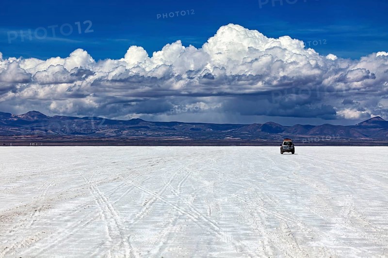 An off-road vehicle drives across an endless salt flat under a sky full of clouds, The endless expanses of the salt plain of the Salar de Uyuni in Bolivia