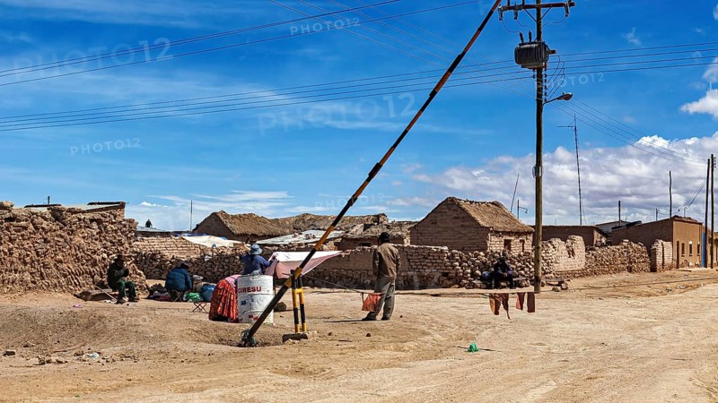 Small desert town with clay-like houses under a blue sky, power lines and local people, A village on the Altiplano plateau in Bolivia