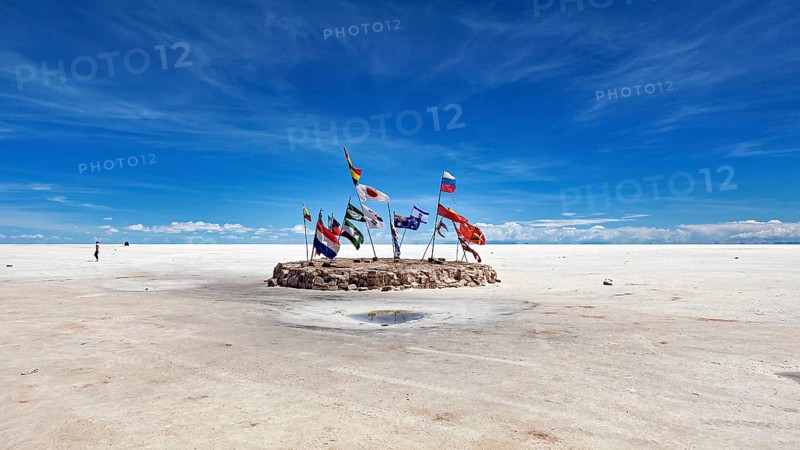 Flags in a vast salt lake under a clear blue sky with scattered clouds, international flags in the vastness of the salt plain of the Salar de Uyuni in Bolivia