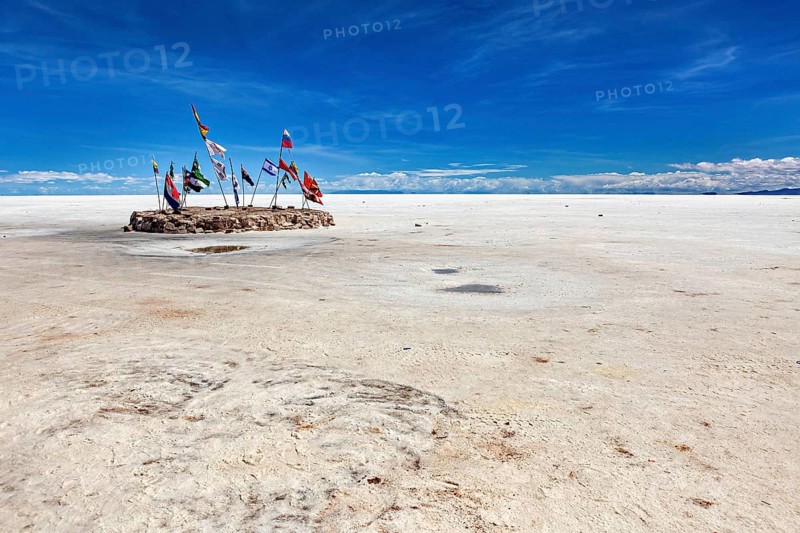 Flags in a vast salt lake under a clear blue sky with scattered clouds, international flags in the vastness of the salt plain of the Salar de Uyuni in Bolivia