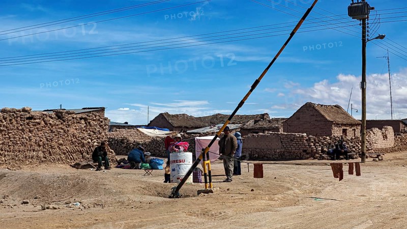 People in a desert town with clay-like buildings and a street lamp under a blue sky, A village on the Altiplano plateau in Bolivia