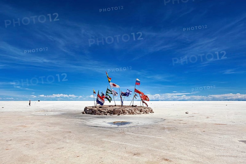 Flags in a vast salt lake under a clear blue sky with scattered clouds, international flags in the vastness of the salt plain of the Salar de Uyuni in Bolivia