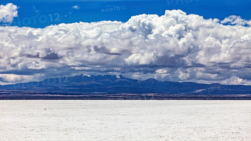 Majestic cloud formation over a flat, white salt landscape with a mountain backdrop, The endless expanses of the salt plain of the Salar de Uyuni in Bolivia