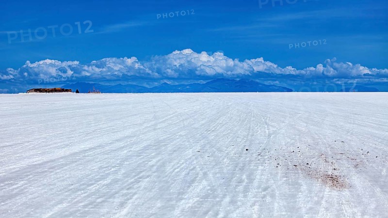 Vast salt flat with a mountain range on the horizon and clouds under a clear sky, The endless expanses of the Salar de Uyuni salt flat in Bolivia