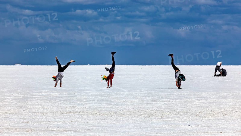 People doing handstands on a vast salt flat under a dramatic sky, The endless expanses of the salt plain of the Salar de Uyuni in Bolivia