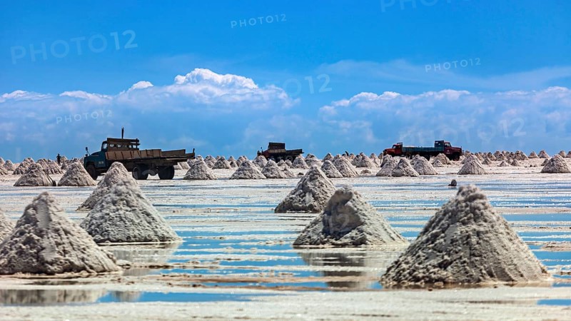 Lorries and salt hills on a reflective salt flat under a blue sky and clouds, The endless expanses of the salt plain of the Salar de Uyuni in Bolivia