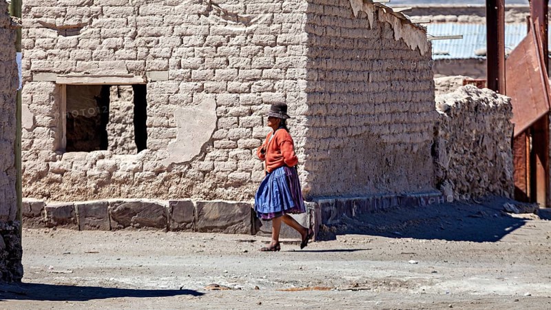 A woman in traditional dress walks along a dusty road in front of adobe houses, Traditional woman in a village in the Salar de Uyuni in Bolivia
