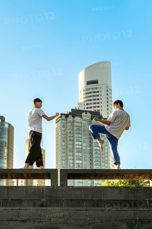 Vertical shot of two young men performing martial arts forms in a city setting