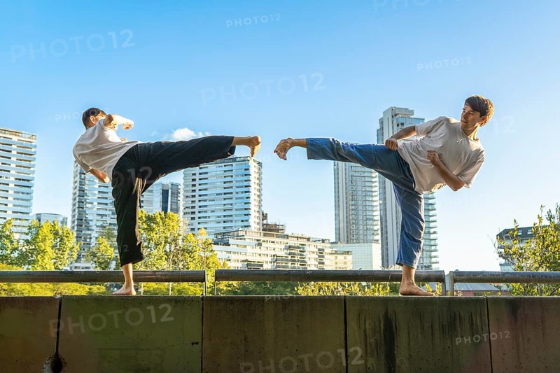 Young men executing synchronized Taekwondo kicks with urban buildings in the background