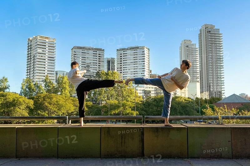 Two young men performing a Taekwondo high kick against a city skyline