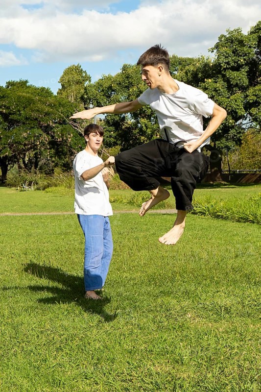Young men practicing dynamic Taekwondo jumps in a park