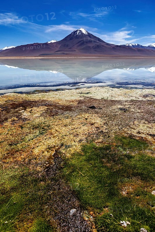 Volcano in front of a clear lake whose surface reflects the summit and the blue sky, The Laguna Colorada in Bolivia