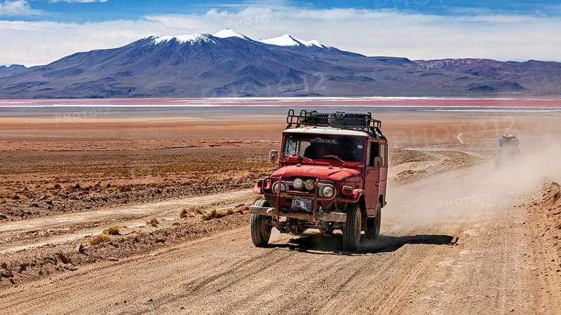 A jeep drives dusty on a desert road with mountains in the background, off road in the landscape of the Altiplano in Bolivia