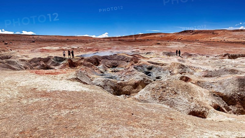 Landscape with geysers in a desert, two people on the horizon, clear blue sky, The mud volcanoes and fumaroles on the Altiplano in Bolivia