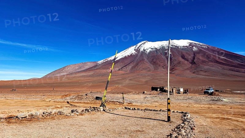 Border area in a treeless desert landscape with a snow-capped mountain and clear blue sky, The border control between bolivia and Chile