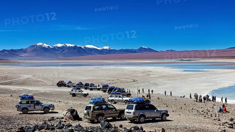 Several off-road vehicles parked in a desert landscape with mountains and snow-capped peaks under a clear sky, Off Road in the Landscape of the Altiplano in Bolivia