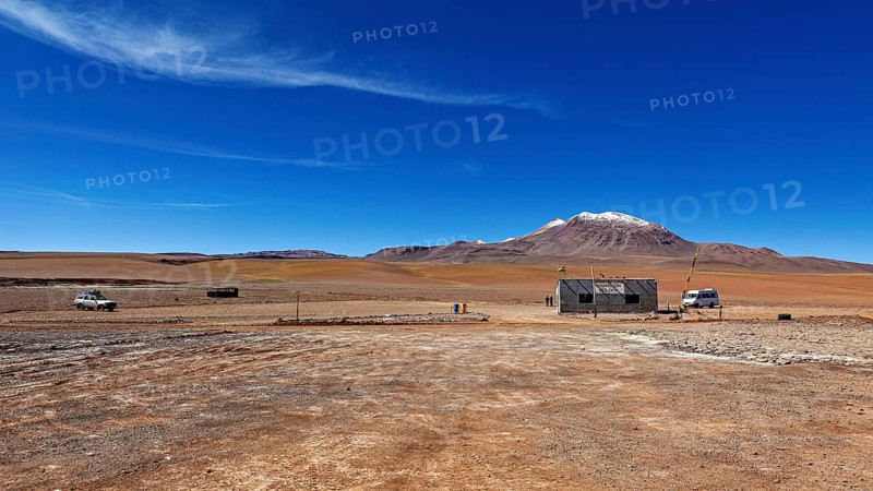 Vast, lonely desert landscape with a small building and snow-capped mountains in the background, The border control between bolivia and Chile
