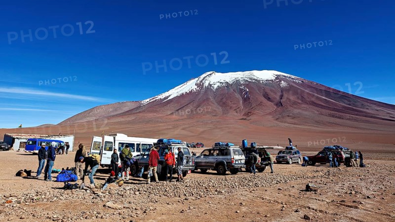 Groups of people and vehicles in a desert landscape with a snow-covered mountain under a blue sky, Off Road in the Landscape of the Altiplano in Bolivia