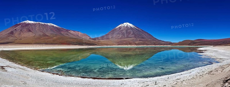Broad mountain backdrop with two snow-covered peaks reflected in a calm lake, The Laguna Colorada in Bolivia