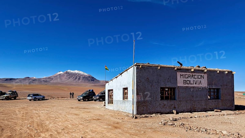 A small border building in a barren landscape with snow-capped mountains in the background, The border control between bolivia and Chile