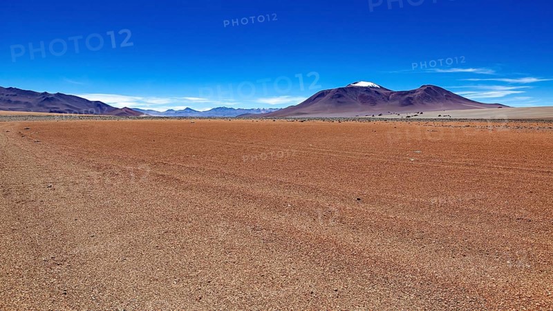 A wide, dry expanse of sand with a mountain on the horizon under a clear blue sky, The landscape of the Altiplano in Bolivia