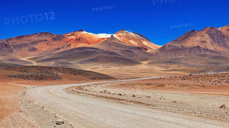 A sandy road winds its way through a vast, barren landscape under a bright blue sky, The landscape of the Altiplano in Bolivia