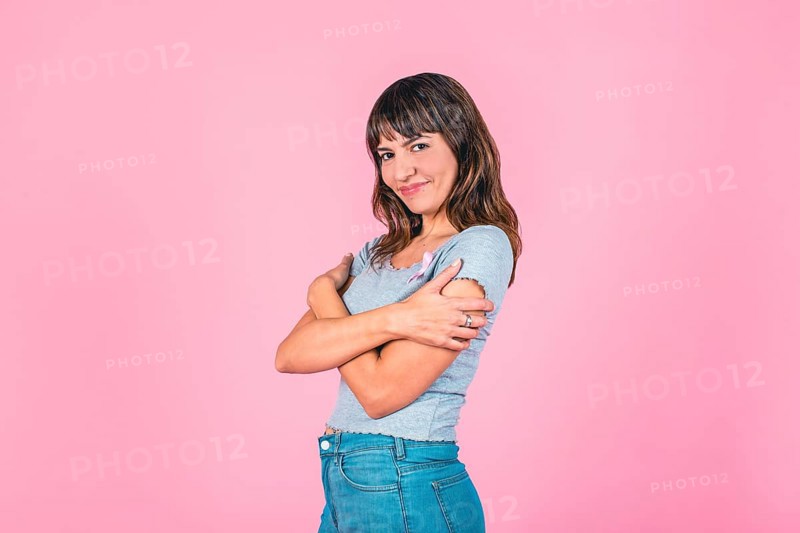 Young woman embracing herself with a pink breast cancer awareness ribbon on a pink backdrop