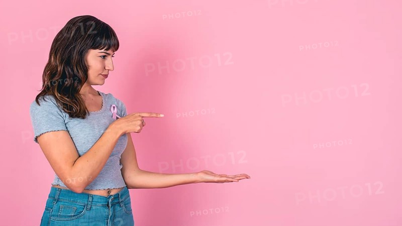 Young woman pointing and presenting with a pink ribbon for breast cancer awareness and copy space