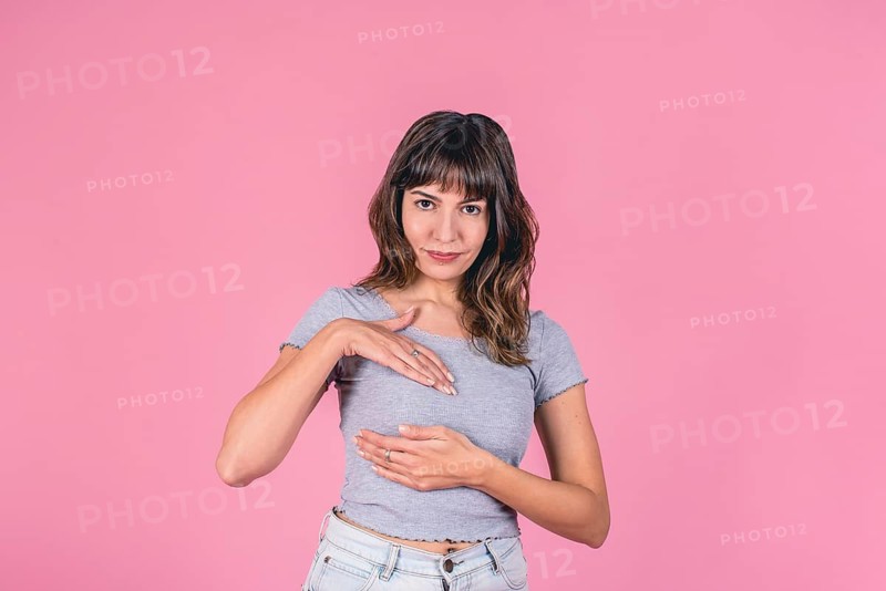 Young woman in gray t-shirt performing breast self-exam on pink background