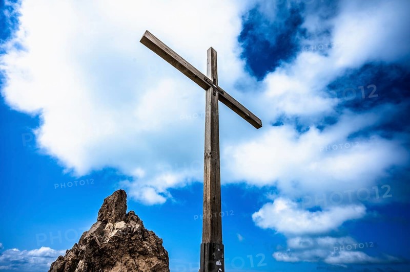 A wooden cross on a rock under a blue sky with white clouds. Kleinwalsertal Vorarlberg Austria Kanzelwand