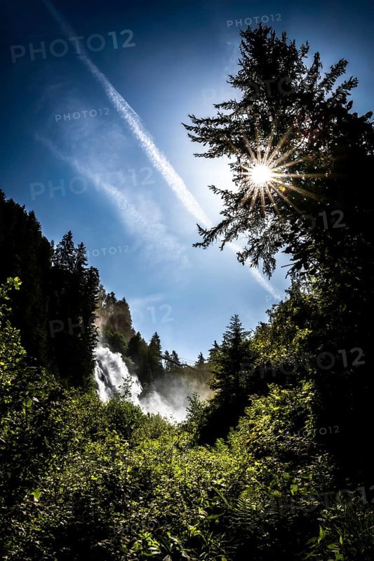 A waterfall in the forest under a bright sun and blue sky. Stuibenfall Austria Ötztal