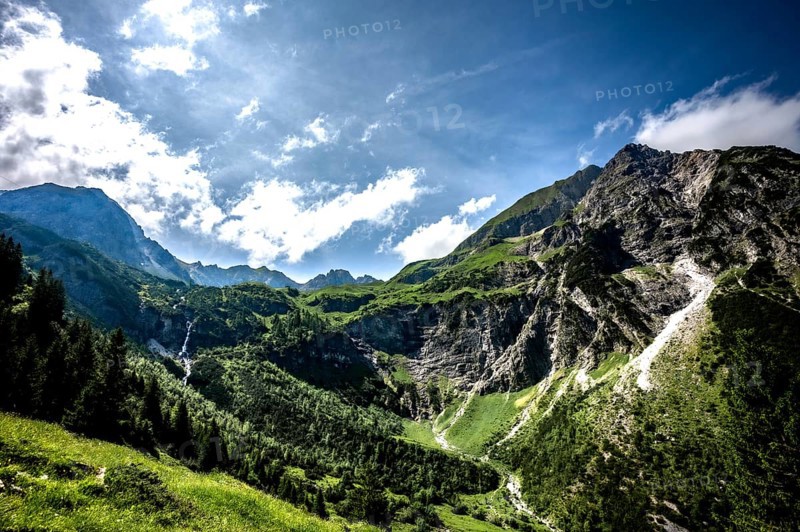 Sunny mountain scene with green slopes and dramatic clouds over the mountains. Kleinwalsertal Vorarlberg Austria