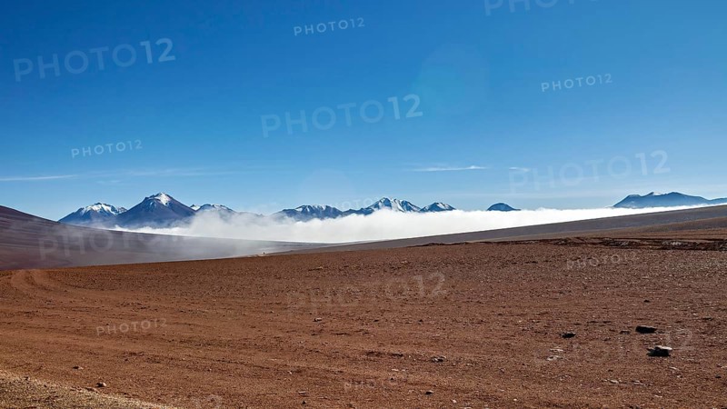 Dry desert plain with distant mountains and wafts of mist under a clear sky, The landscape at San Pedro de Atacama in Chile