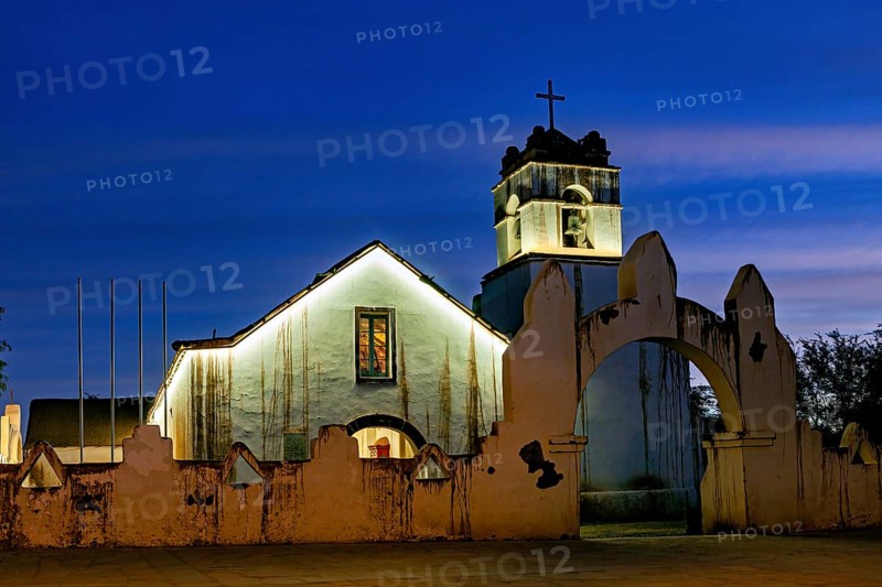 Church at dusk with illuminated tower and cross in front of a deep blue sky, The church of San Pedro de Atacama in Chile