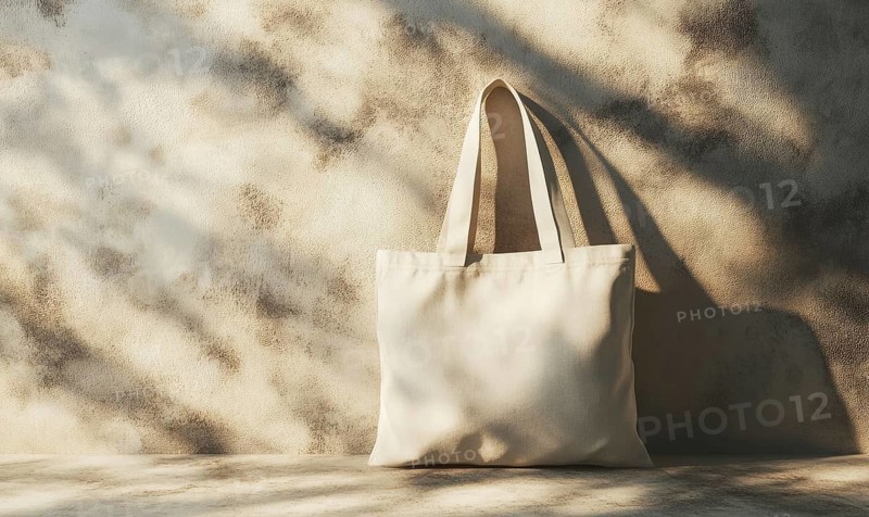 A white canvas bag is sitting on a table in front of a wall. The bag is empty and the wall is made of stone. The scene is simple and uncluttered, with the focus on the bag and the wall. AI generated