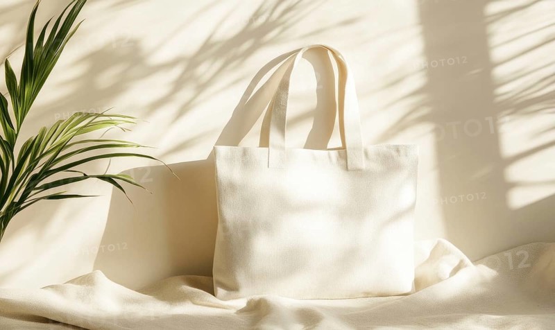 A cream-colored canvas bag placed in soft sunlight with shadows from a plant. AI generated