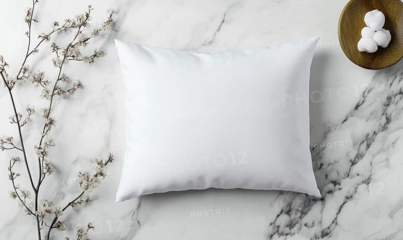 A white pillow sits on a marble countertop. The pillow is unmade and has a floral pattern on it. The countertop is clean and shiny, and there is a bowl of cotton balls on the counter. AI generated