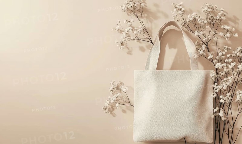 A white tote bag surrounded by delicate white flowers against a soft beige background. AI generated