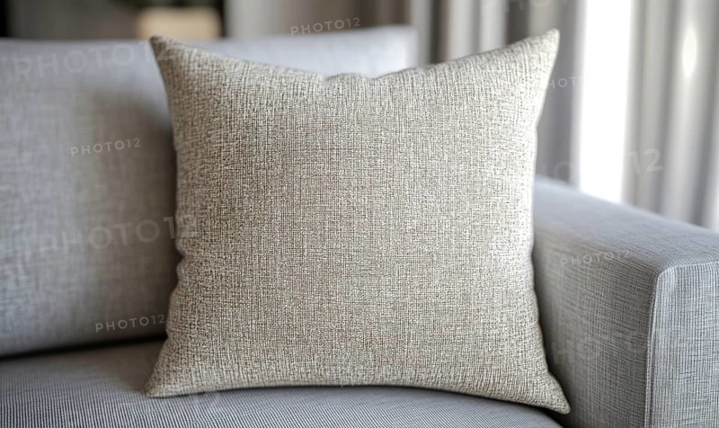 A pillow with a pattern on it sits on a couch. The pillow is white and has a texture that looks like it's made of fabric. AI generated