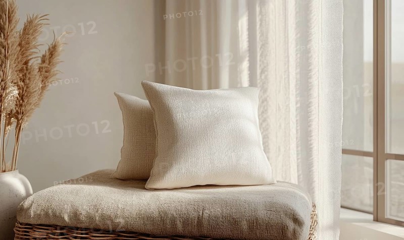 A white pillow sits on a chair in front of a window. The pillow is placed on top of a basket, which is also white. The room has a clean and simple design, with a window that lets in natural light. AI generated