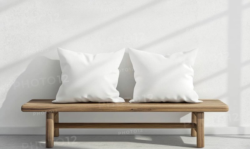 A wooden bench with two white pillows on it. The bench is located in a room with a white wall and a window. The sunlight is shining through the window, creating a warm. AI generated