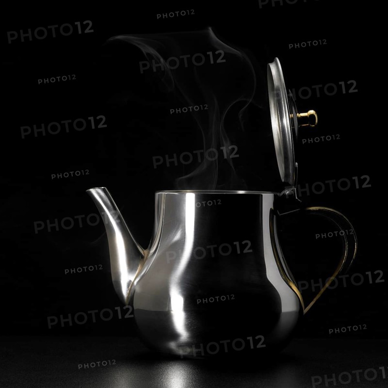 Studio photography of a steaming metal tea pot in dark back
