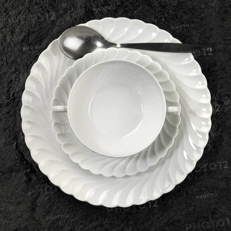 Studio photography of white porcelain plates and spoon on dark stone surface seen from above