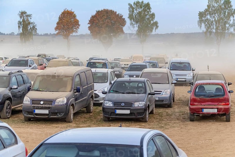 Dusty parking space scenery on a field including lots of dust covered cars at evening time in Southern Germany