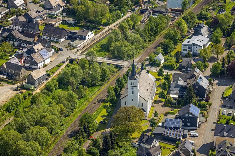 Aerial view, catholic church St. Andreas, residential area Mühlenstraße corner Kanalstraße, railway line level crossing and Ruhr bridge Kanalstraße, river Luchtmücke and greened river Ruhr, residential area, behind the weir Velmede, Velmede, Bestwig, Sauerland, North Rhine-Westphalia, Germany, catholic church, St. Andreas, Mühlenstraße, Kanalstraße, railway line, level crossing, Ruhr bridge, river, Luchtmücke, green river, Ruhr, weir, architecture, religious building, traffic, infrastructure, nature, town, village, bridge, railway, green area, building, perspective, bird's eye view, structure