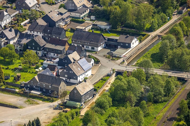 Aerial view, residential area Mühlenstraße corner Kanalstraße, railway line level crossing and Ruhr bridge Kanalstraße, green river Ruhr, behind the weir Velmede, Velmede, Bestwig, Sauerland, North Rhine-Westphalia, Germany, residential area, Mühlenstraße, Kanalstraße, railway line, railway crossing, Ruhr bridge, green river, Ruhr, weir, river landscape, infrastructure, bridge, railway, traffic routes, settlement, houses, streets, water, nature, aerial view, urban planning, region, geographical, european, scenic, urban, architecture, environment, riverbank