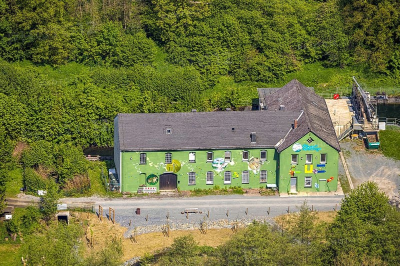 Aerial view, Altes Wasserkraftwerk Alfert, NaturRanger e.V., and green house painted with animals and plants, Ostwig, Bestwig, Sauerland, North Rhine-Westphalia, Germany, old hydroelectric power station, Alfert, painted house, green house, plants, animals, art, mural, building, architecture, nature, environmental protection, landscape, rural, wooded, picturesque, historic buildings, conscious decoration, culture, environment, bird's eye view, village, bank, river, energy, sustainability